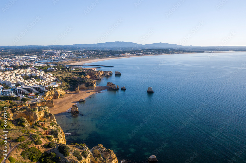 Dona Ana beach at sunrise. Portuguese southern golden coast cliffs. Aerial view over city of Lagos in Algarve, Portugal.