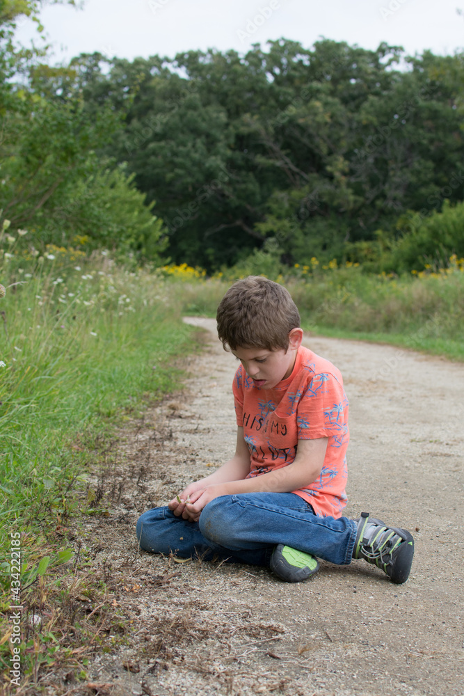 Young boy with Autism sitting on walking path playing with rocks Young boy with Autism sitting on walking path playing with rocks