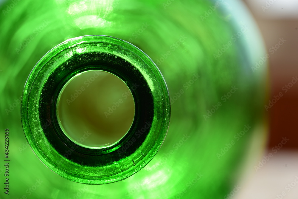 Close-up of an green glass bottle, illuminated by sunlight from behind. A look inside the large neck.