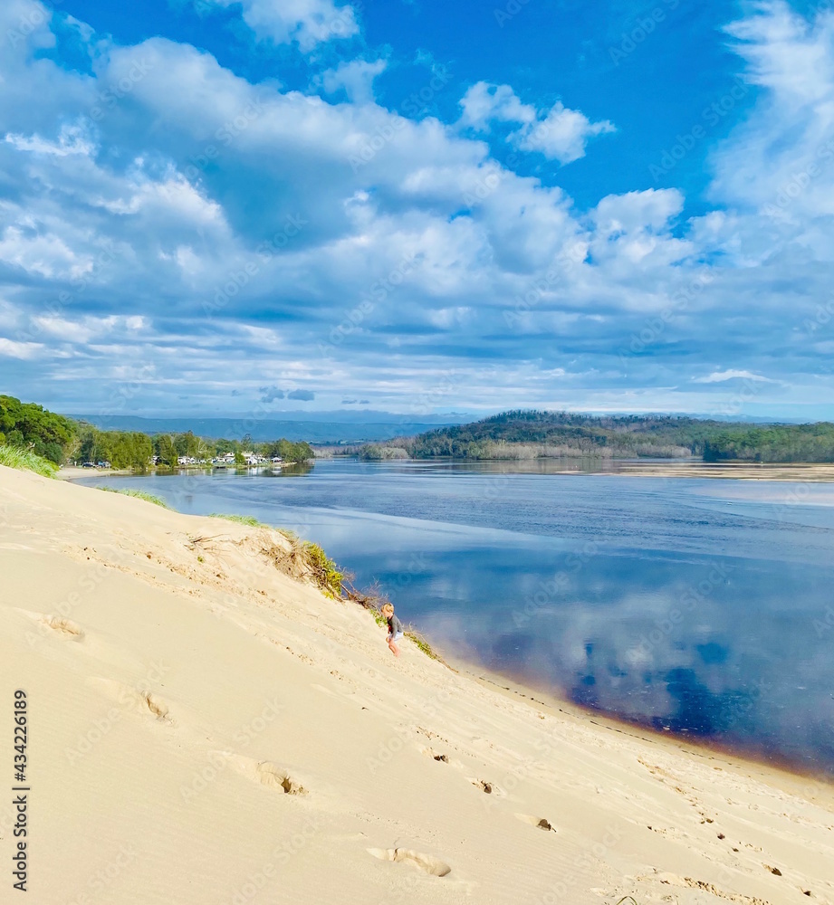 Child climbing up sand dune with lake in view Child climbing up sand dune with lake in view