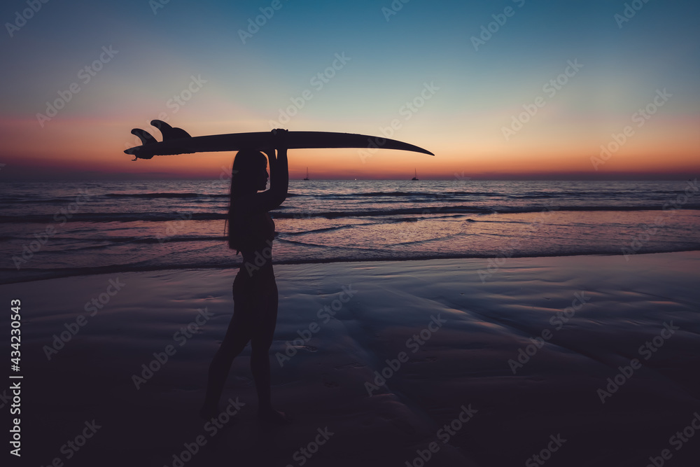 Silhouette of beautiful sexy surfer female with surfboard on the sandy beach at sunset. water sports. Surfing are healthy active lifestyle. Summertime vacation.