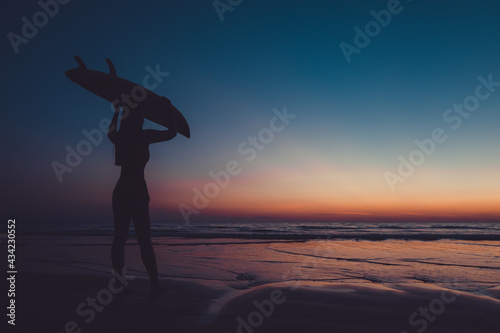 Silhouette of beautiful sexy surfer female with surfboard on the sandy beach at sunset. water sports. Surfing are healthy active lifestyle. Summertime vacation.