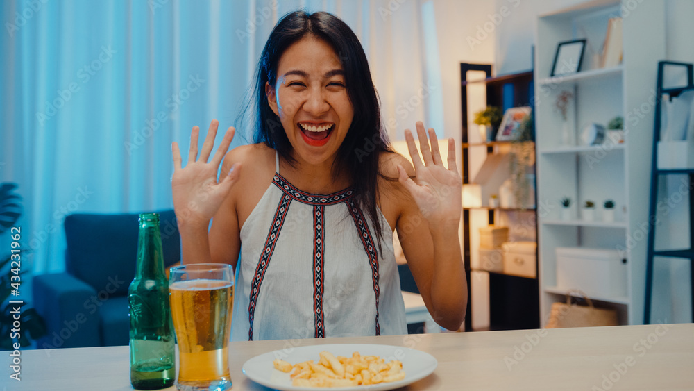 Young Asia lady drinking beer having fun happy night party New Year event online celebration via video call by phone at home at night. Social distance, quarantine for coronavirus. Point of view or POV Young Asia lady drinking beer having fun happy night party New Year event online celebration via video call by phone at home at night. Social distance, quarantine for coronavirus. Point of view or POV