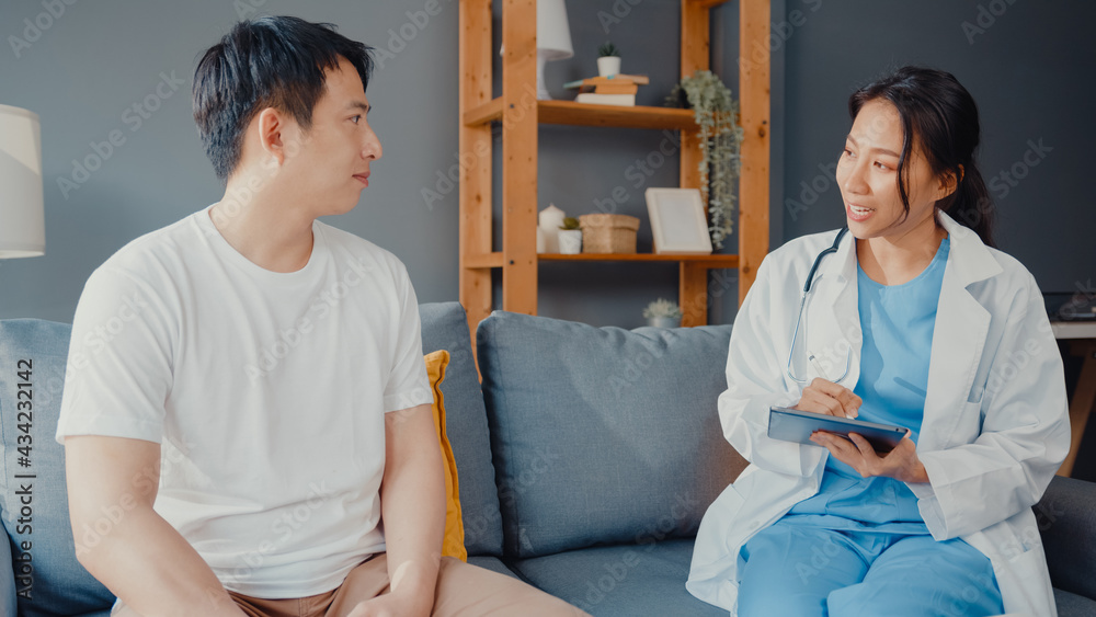 Fototapeta premium Young Asia female professional physician doctor using digital tablet sharing good health test news with happy male patient sit on couch in house. Medical insurance, Visit patient at home concept.
