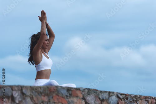 Asian young woman practicing yoga sitting in lotus position. Easy yoga poses for beginners. Exercise while looking out to the sea. Stretching & Strengthening Exercises with yoga.