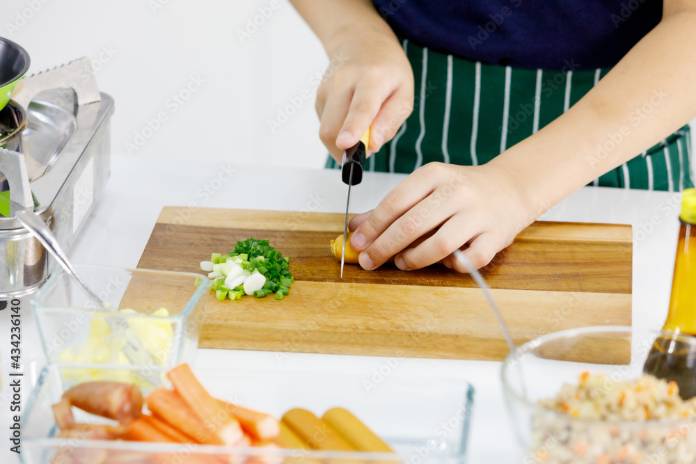 Cropped photo of kid learn to cook healthy food for family in modern home kitchen by using knife slice food on wooden plate into pieces. Cropped photo of kid learn to cook healthy food for family in modern home kitchen by using knife slice food on wooden plate into pieces.