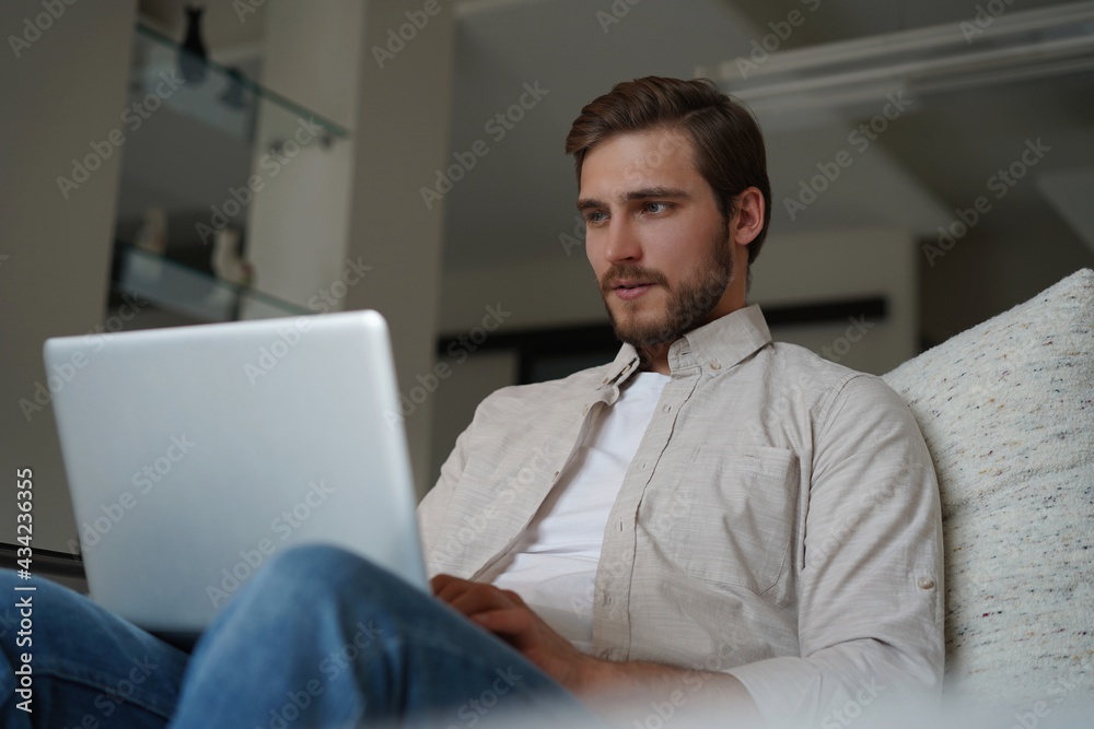 Man using laptop, sitting on couch at home, chatting or shopping in internet, freelancer working online Man using laptop, sitting on couch at home, chatting or shopping in internet, freelancer working online