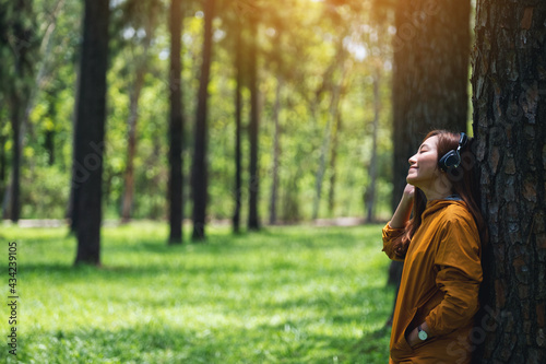 Portrait image of a beautiful young asian woman enjoy listening to music with headphone in the park