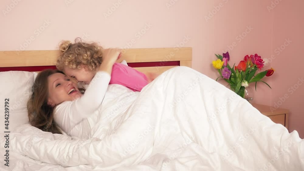 cheerful cuddly girl wake her young mother in bed. 4K cheerful cuddly girl wake her young mother in bed. 4K