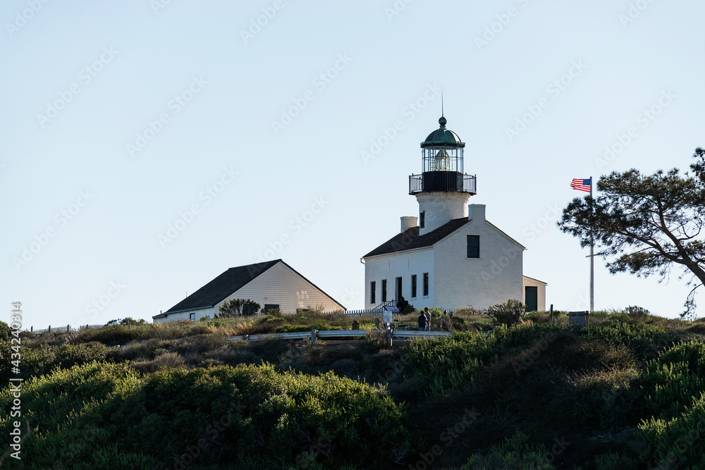 Historic Old Point Loma Lighthouse and outbuilding at Cabrillo National Monument in San Diego, California from a low angle with a pale blue sky in the background.