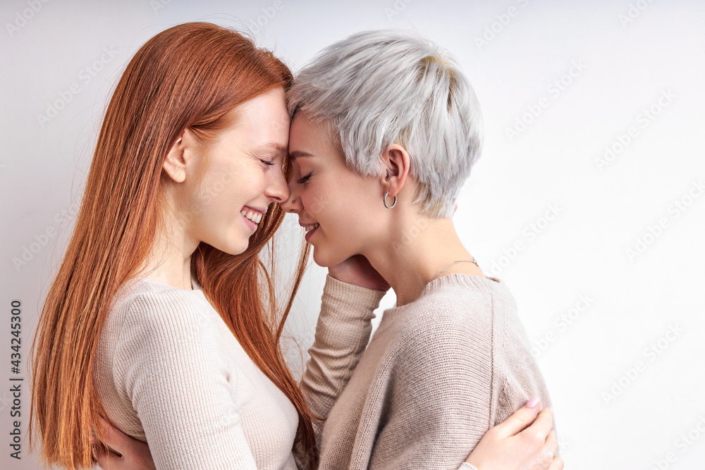 Side View Portrait Of Pretty Redhead Woman And Short Haired Lady Hugging, Feeling Love, Standing Closely To Each Other, Enjoying Time Together, Smiling Happily. LGBT, Lesbians, lgbt couple Side View Portrait Of Pretty Redhead Woman And Short Haired Lady Hugging, Feeling Love, Standing Closely To Each Other, Enjoying Time Together, Smiling Happily. LGBT, Lesbians, lgbt couple