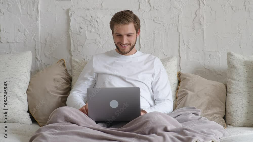 Cheerful caucasian man sits at home on the couch and works using a laptop, financial manager on a remote work during self-isolation in quarantine, a man makes a good deal, positive emotions. Cheerful caucasian man sits at home on the couch and works using a laptop, financial manager on a remote work during self-isolation in quarantine, a man makes a good deal, positive emotions.