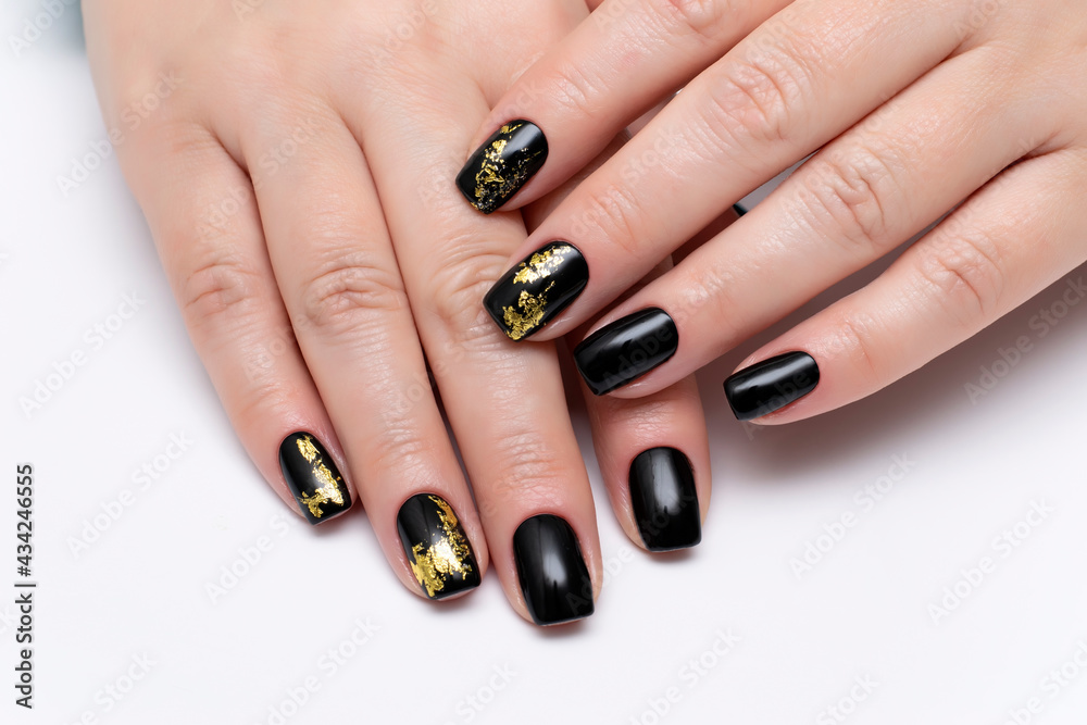 Black manicure on short square nails close-up on a white background with gold foil. Black manicure on short square nails close-up on a white background with gold foil.
