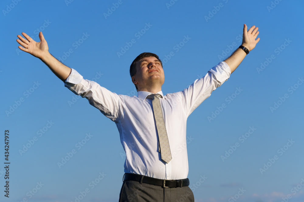 businessman poses in a field, he looks into the distance and rests, green grass and blue sky as background businessman poses in a field, he looks into the distance and rests, green grass and blue sky as background