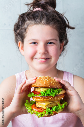 Brunette teenage girl smiling and holding big vegan burger in her hands.