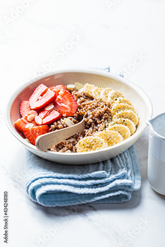 Buckwheat porridge with banana, strawberries and maple syrup in white bowl. Healthy breakfast concept.