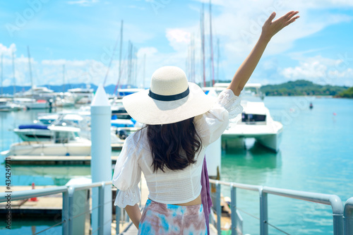Excited tourist in white hat enjoying and standing on the dock with luxury yachts during summer