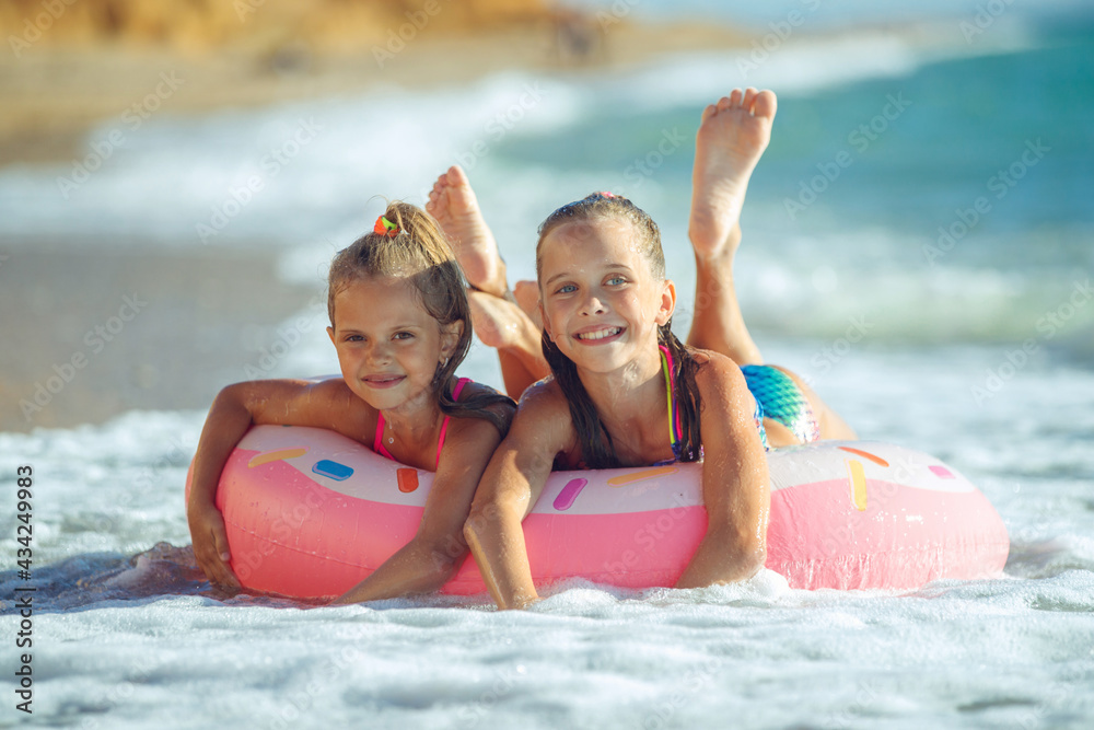 Obraz premium Children are playing on the beach. Children swim and play in the sea on summer family vacations. Sand and water activities. Two girls run on the ocean shore. High quality photo.