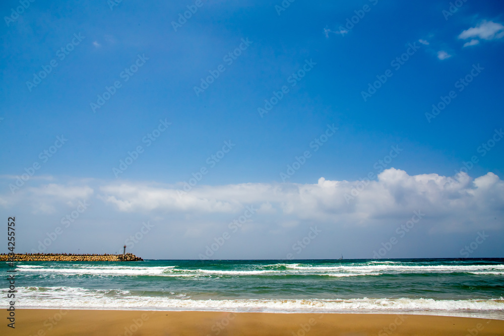 Seashore or ocean, golden sand, blue sea and low distant clouds on a sunny day, place for text, background