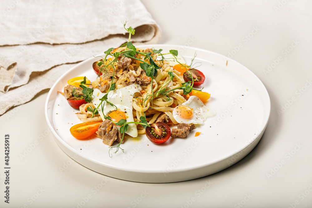 Close-up of delicious homemade spaghetti with vegetables, cheese and fried quail eggs on a round plate on a light background. Traditional Italian food. Mediterranean lunch or dinner. Close-up of delicious homemade spaghetti with vegetables, cheese and fried quail eggs on a round plate on a light background. Traditional Italian food. Mediterranean lunch or dinner.