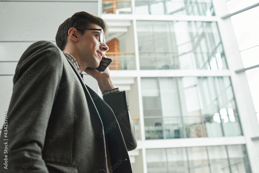 Young businessman in suit walking along the city and talking on mobile phone