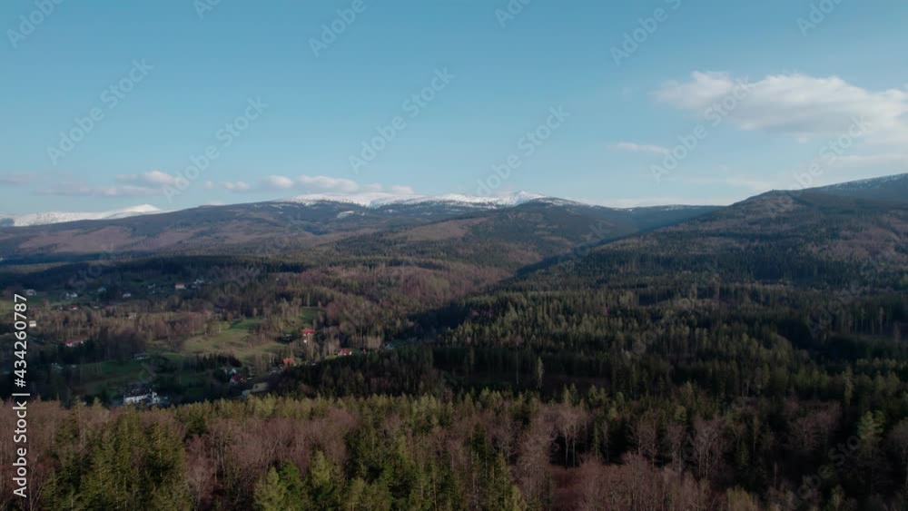 A view of the forested hills and the mountains covered with snow on the horizon. Drone flight over forests in the mountains. A view of the forested hills and the mountains covered with snow on the horizon. Drone flight over forests in the mountains.