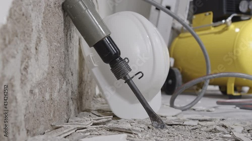 house renovation concept, wall in demolition with plaster rubble and protective construction work tools, helmet, yellow compressor and pneumatic air hammer chisel, close up on floor