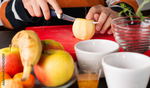 Blurred image of fruit in the foreground in the background a boy cuts an apple for making fruit salad.