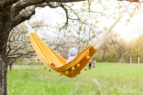 Child in a yellow hammock under a tree in a green landscape.Kind in gelber Hängemate unter Baum in grüner Landschaft.
