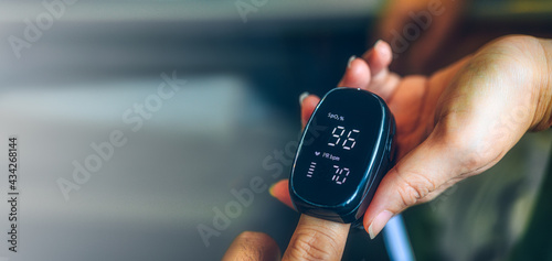 Hand of asian woman with an attached pulse oximeter on fingertip, checking oxygen saturation level in the blood,diagnosis of Coronavirus or COVID-19 at home,health care