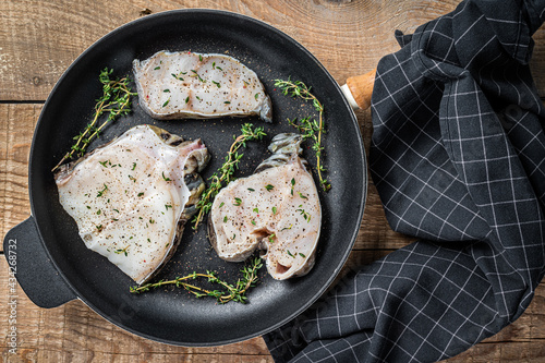 Fresh raw wolffish fillet steaks in a pan with herbs. wooden background. Top view