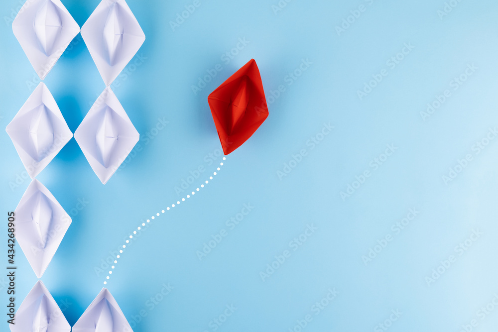 A group of white paper ship pointing in one direction and one red paper ship. Business behind an innovative solution concept.