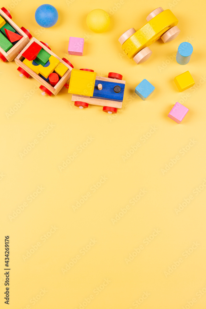 Baby kids toys. Wooden train, car, colorful blocks and balls on yellow background. Top view, flat lay