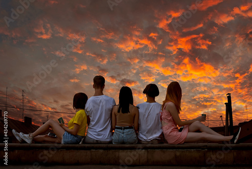 Silhouette of friends sitting on the curb and looking at the sky. Sunset and orange sky in the background. The concept of friendship and joy.