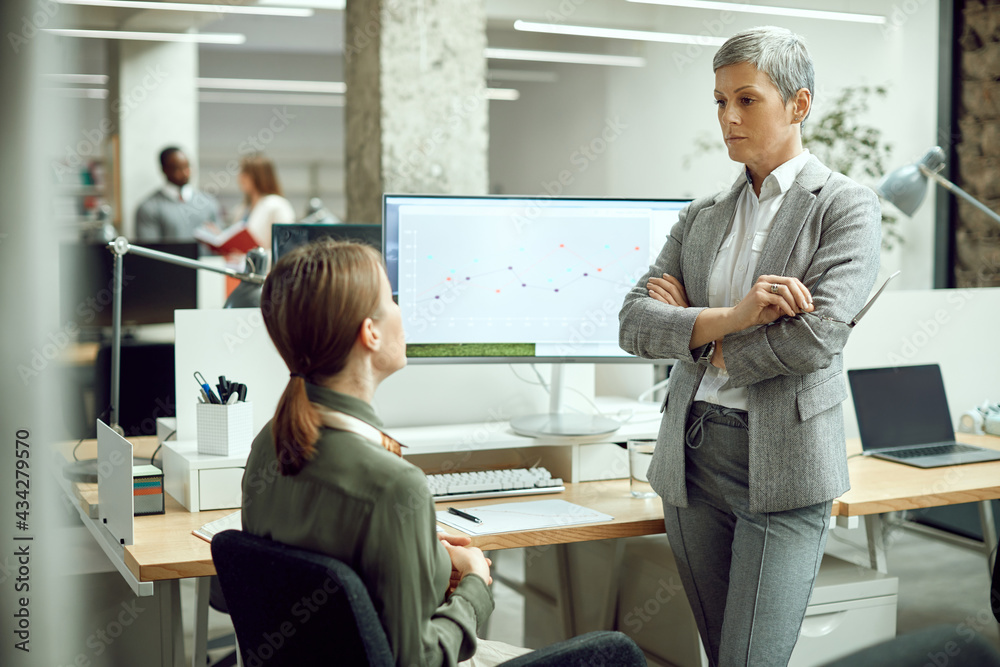 Obraz premium Dissatisfied CEO standing with arms crossed while communicating with her employee at corporate office.