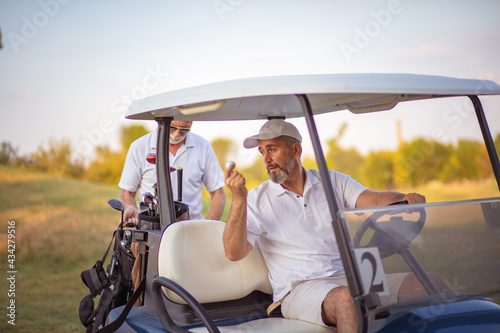 Two senior men golfers on court. Man sitting in golf cart.  Two senior men golfers on court. © liderina