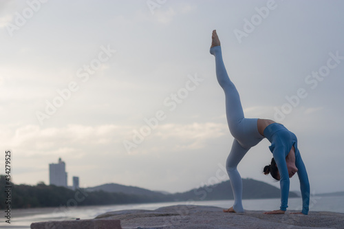 Young attractive Asian woman practicing yoga on the beach.