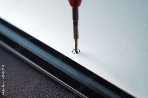 Close up - master unscrewing small screw with screwdriver tool, disassembling and repairing of broken silver laptop. Concept of repair or technical service notebook.