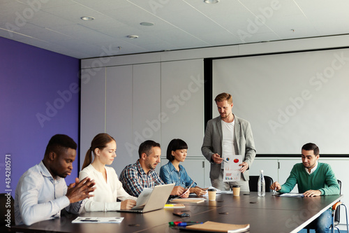 Group of diverse business people having meeting in conference room. Middle aged male manager presenting marketing report with data and graphs to collegaues sitting at table photo