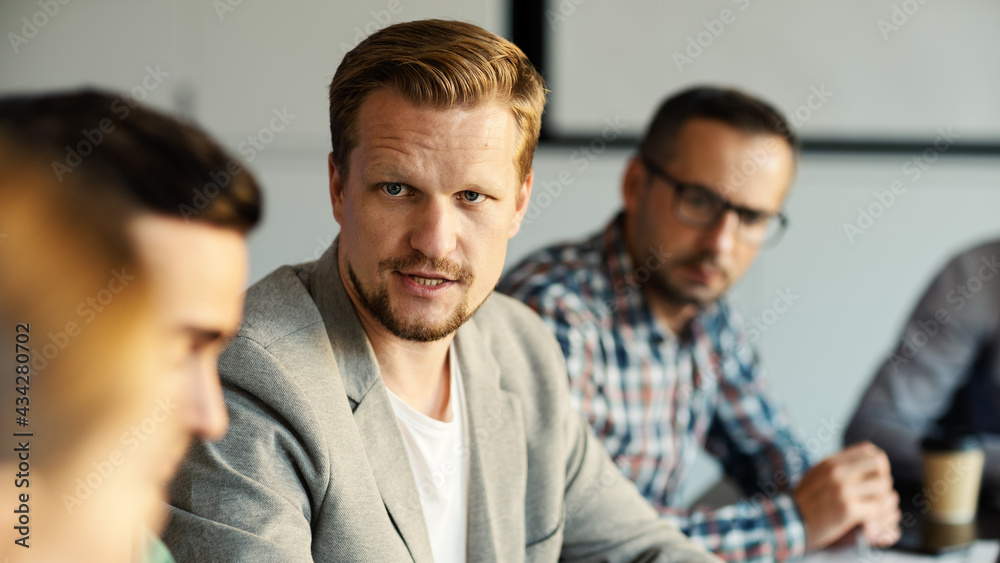 Selective focus of Caucasian middle aged man talking to colleagues expressing his opinion in business meeting or at conference