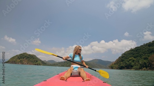 Sportive woman rows pink plastic canoe along sea water. Positive sports girl hand padding on kayak  front view.