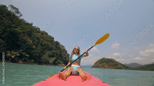 Sportive woman rows pink plastic canoe along sea water. Positive sports girl hand padding on kayak, front view.