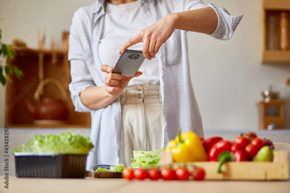 Woman taking photo of healthy salad with smartphone for her blog on kitchen at home Woman taking photo of healthy salad with smartphone for her blog on kitchen at home