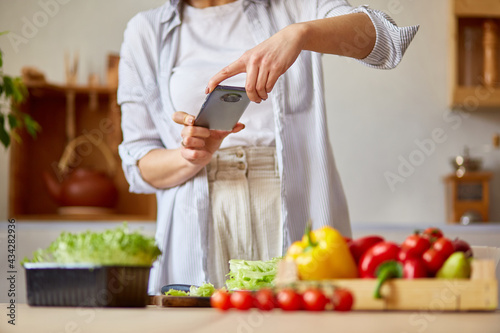 Woman taking photo of healthy salad with smartphone for her blog on kitchen at home