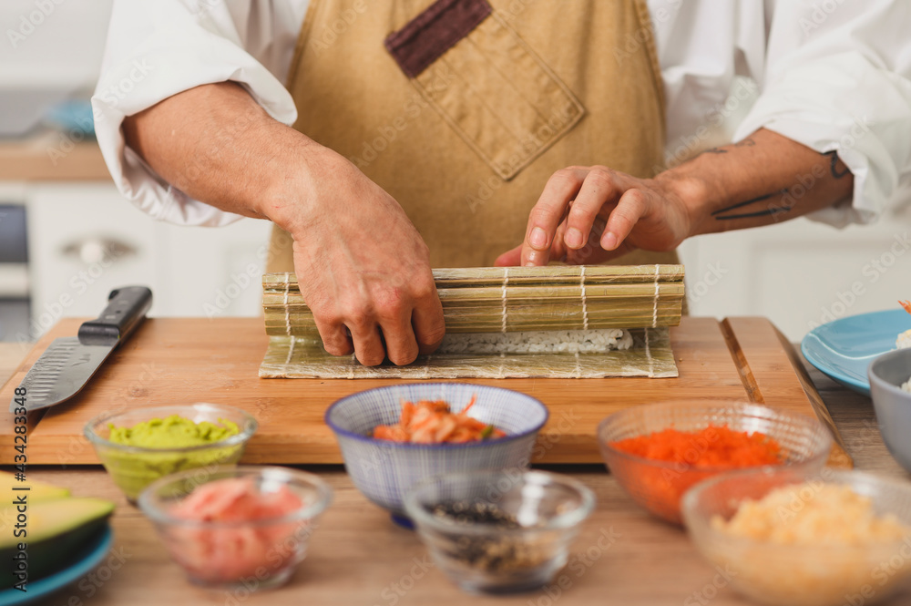 Asian chef hands rolling sushi with bamboo mat. Sushi preparation process with ingredients. Japan food delivery background