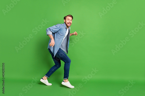 Full length body size photo of thief sneaking away looking back scared afraid stole something isolated vibrant green color background photo