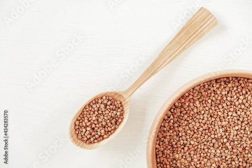 Buckwheat kernels in wooden bowl and spoon on white background. Top view. Copy, empty space for text