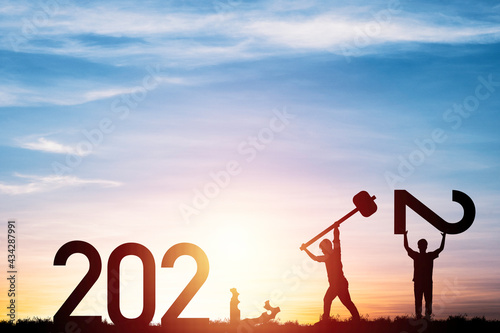 Silhouette man use hammer for knocking to destroy number one and one man raised number two for changing 2021 to 2022 with cloudy sky and sun light , Happy new year preparation concept.