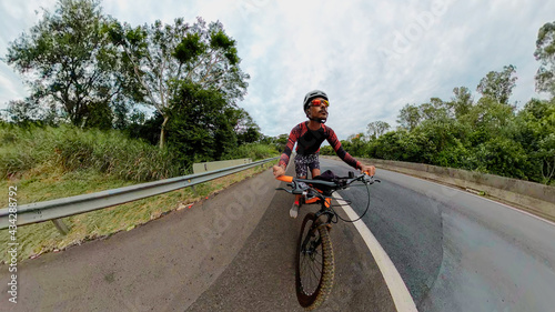 Black man with helmet and glasses riding a bicycle on the road. Space for text.