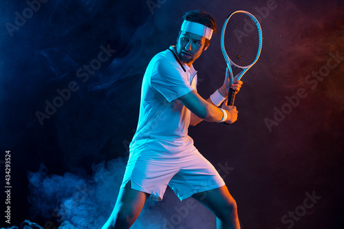 Tennis player with racket in white t-shirt. Man athlete playing on dark background. © Mike Orlov